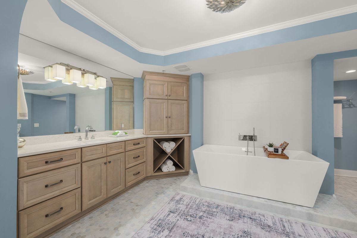 Primary bath with a freestanding white tub, a light wood vanity and soft blue walls