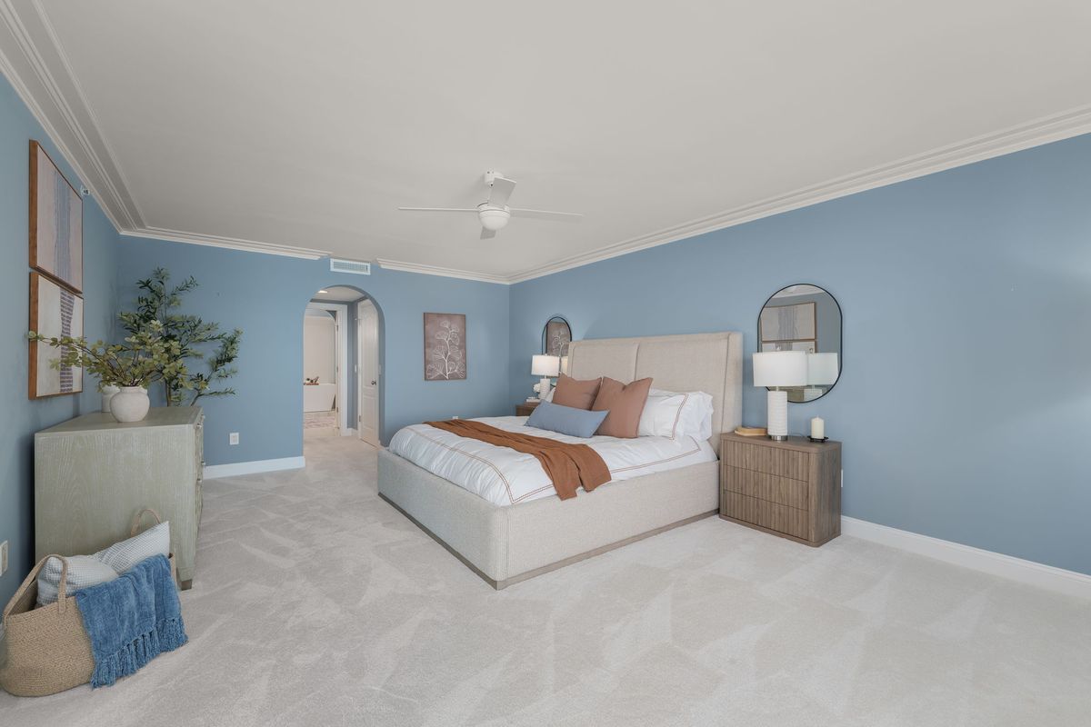 Primary bedroom with soft blue walls, an upholstered bed with rust and white bedding, and wood nightstands