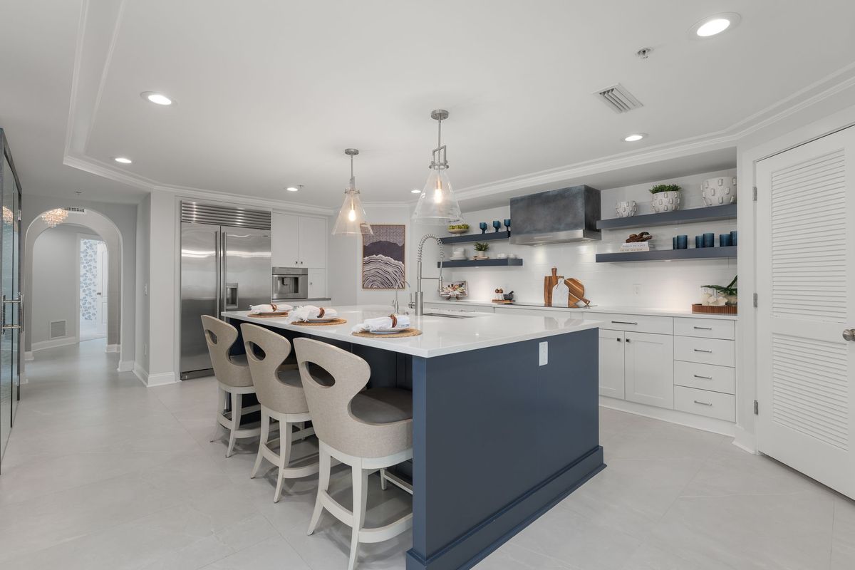 Kitchen with a navy island, white counter stools, glass pendant lights and open shelving