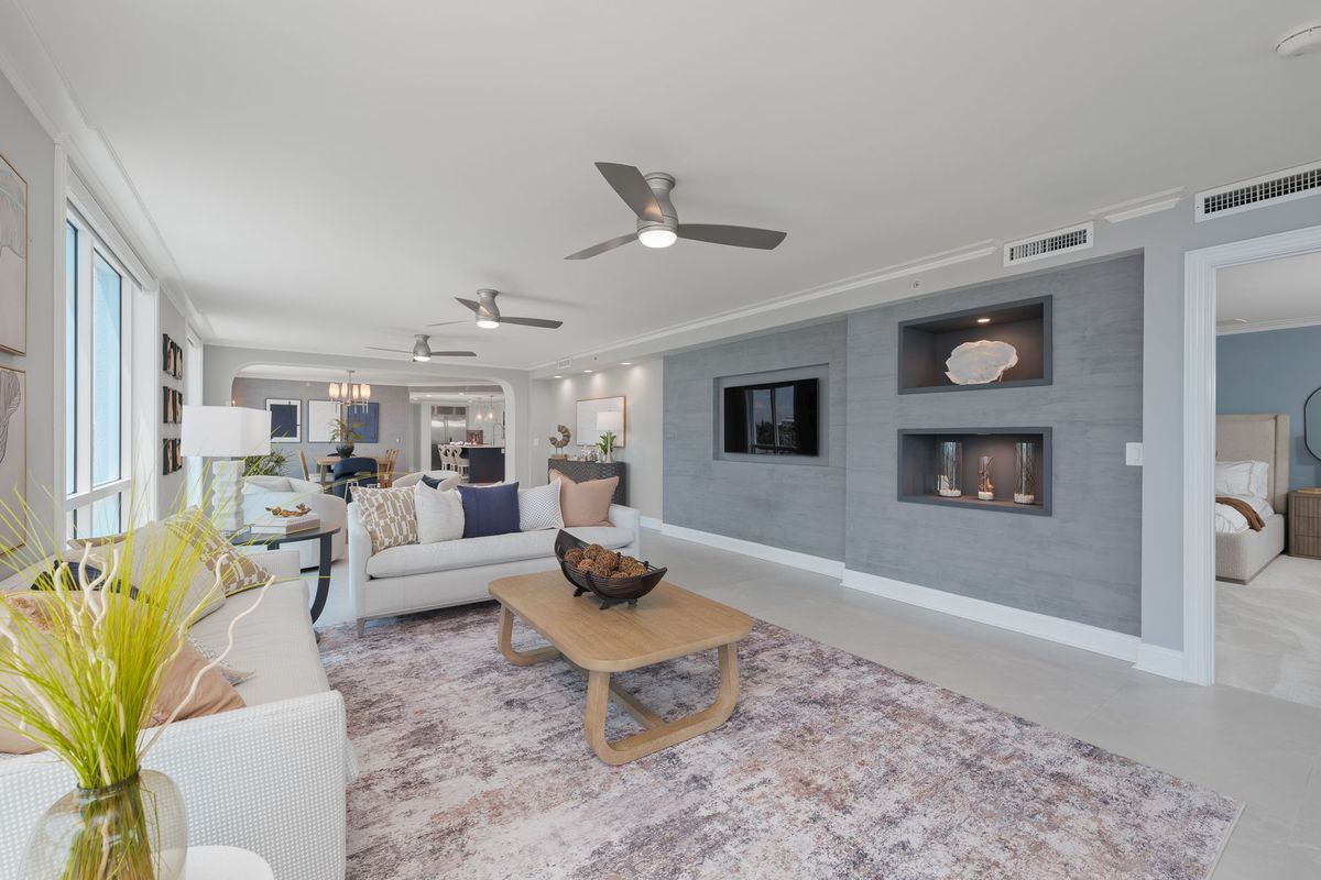 Long living space with a gray accent wall with lit niches, a sectional sofa, a patterned rug and ceiling fans