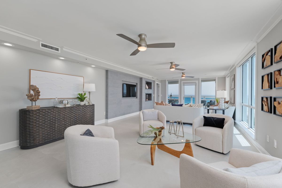 Sitting area with white swivel chairs and a glass coffee table, with ocean-view windows at the far end