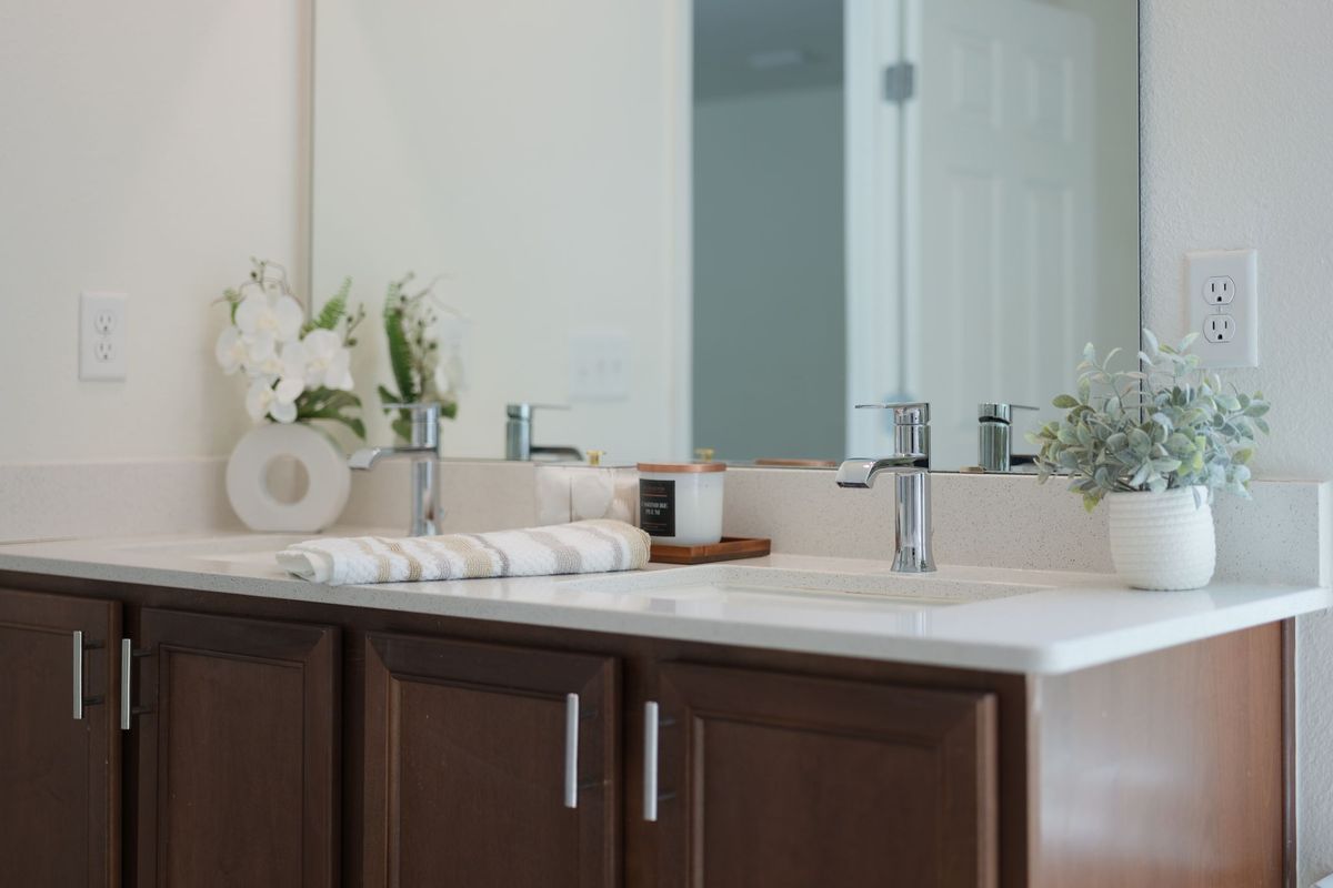 Bathroom vanity with dark wood cabinets and a white counter, styled with a white orchid, a small potted plant and rolled towels