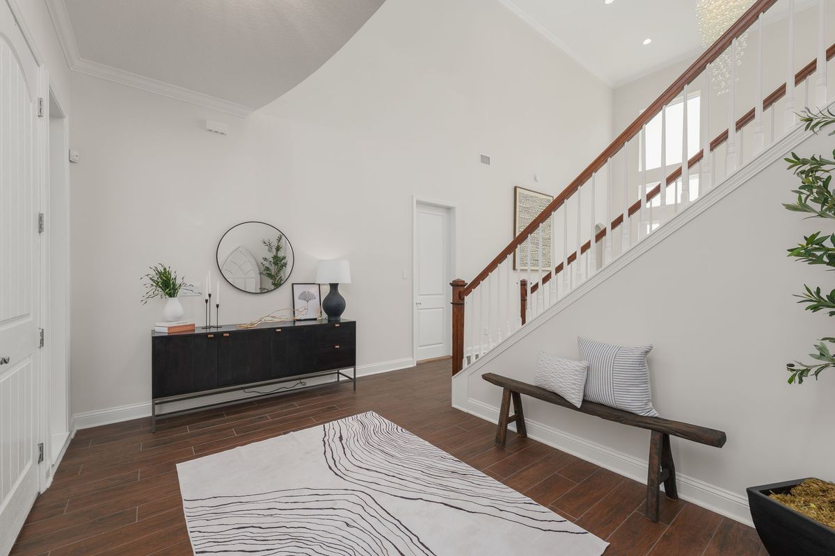 Entry foyer with a staircase, a wooden bench, a black console with a round mirror and a patterned rug