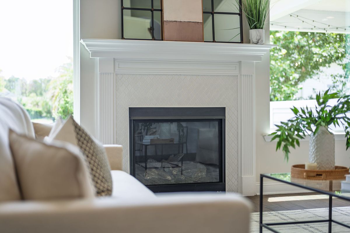 Close-up of a white fireplace mantel beside a sofa with linen pillows and a leafy plant