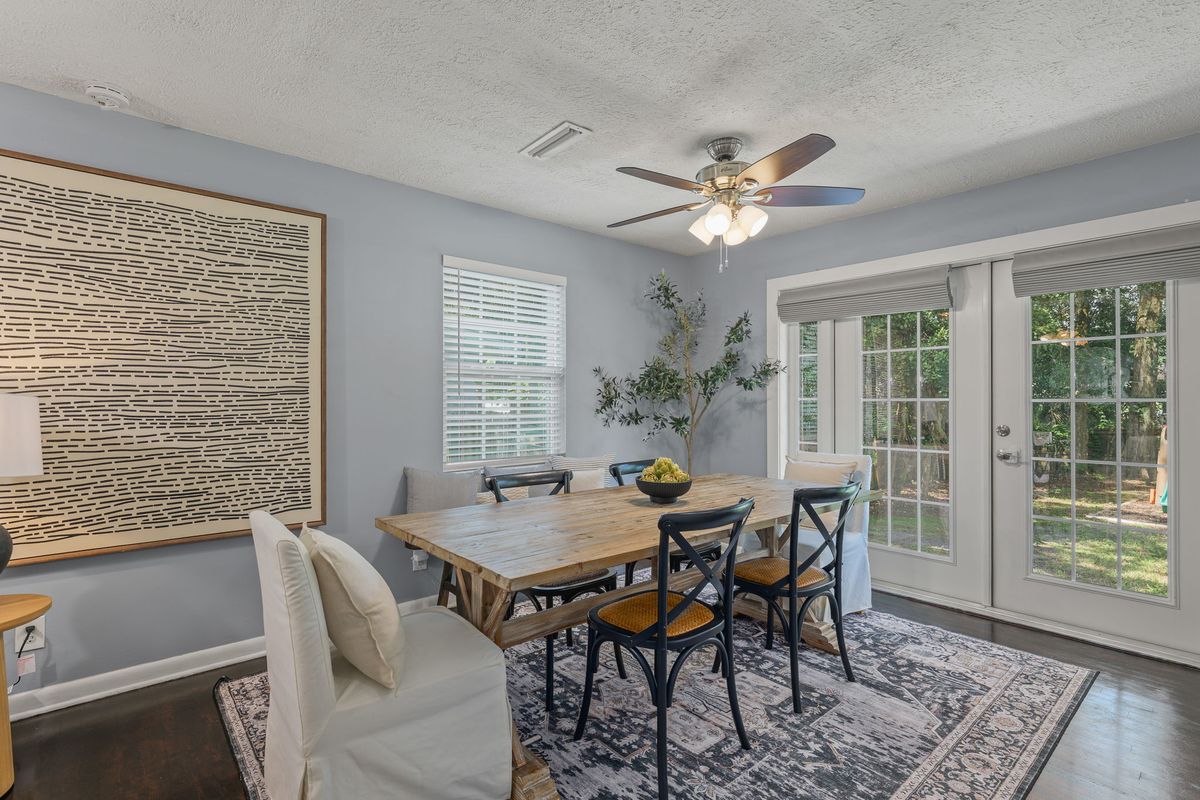 Farmhouse dining table with black spindle chairs on a blue rug, beside French doors and a large abstract artwork