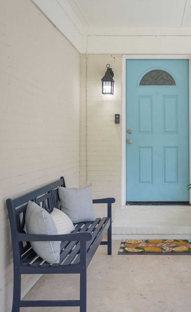 Covered front porch with a turquoise front door, a lantern and a navy bench with striped pillows