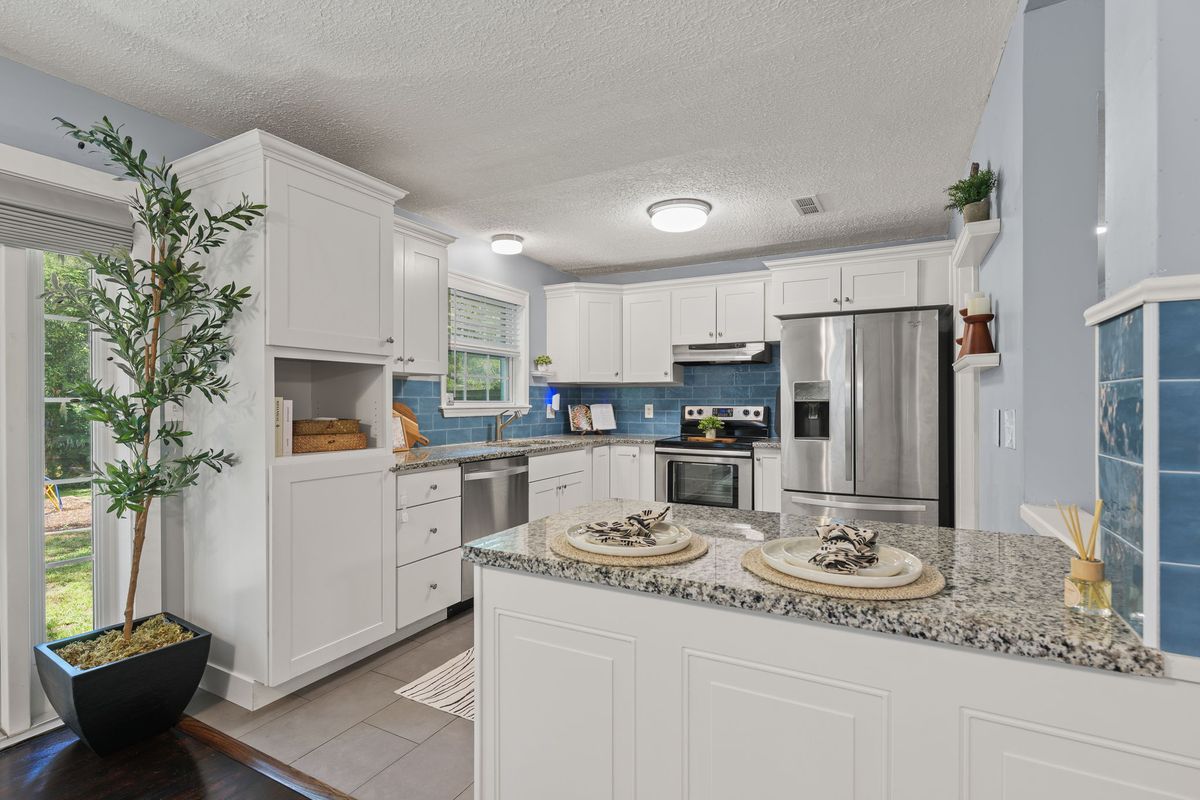White kitchen with a granite peninsula, stainless appliances and a blue tile backsplash