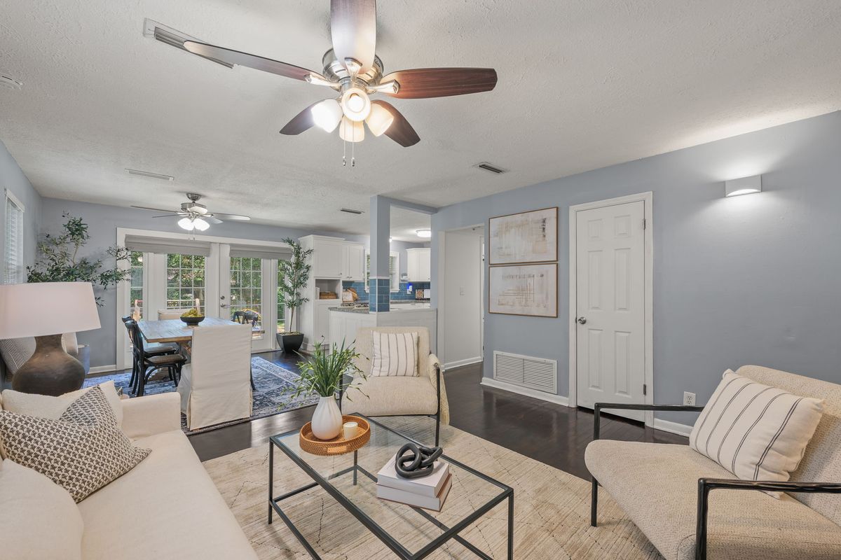 Living room with soft blue walls, an ivory sofa, a pair of cream armchairs and a glass coffee table, open to the dining area