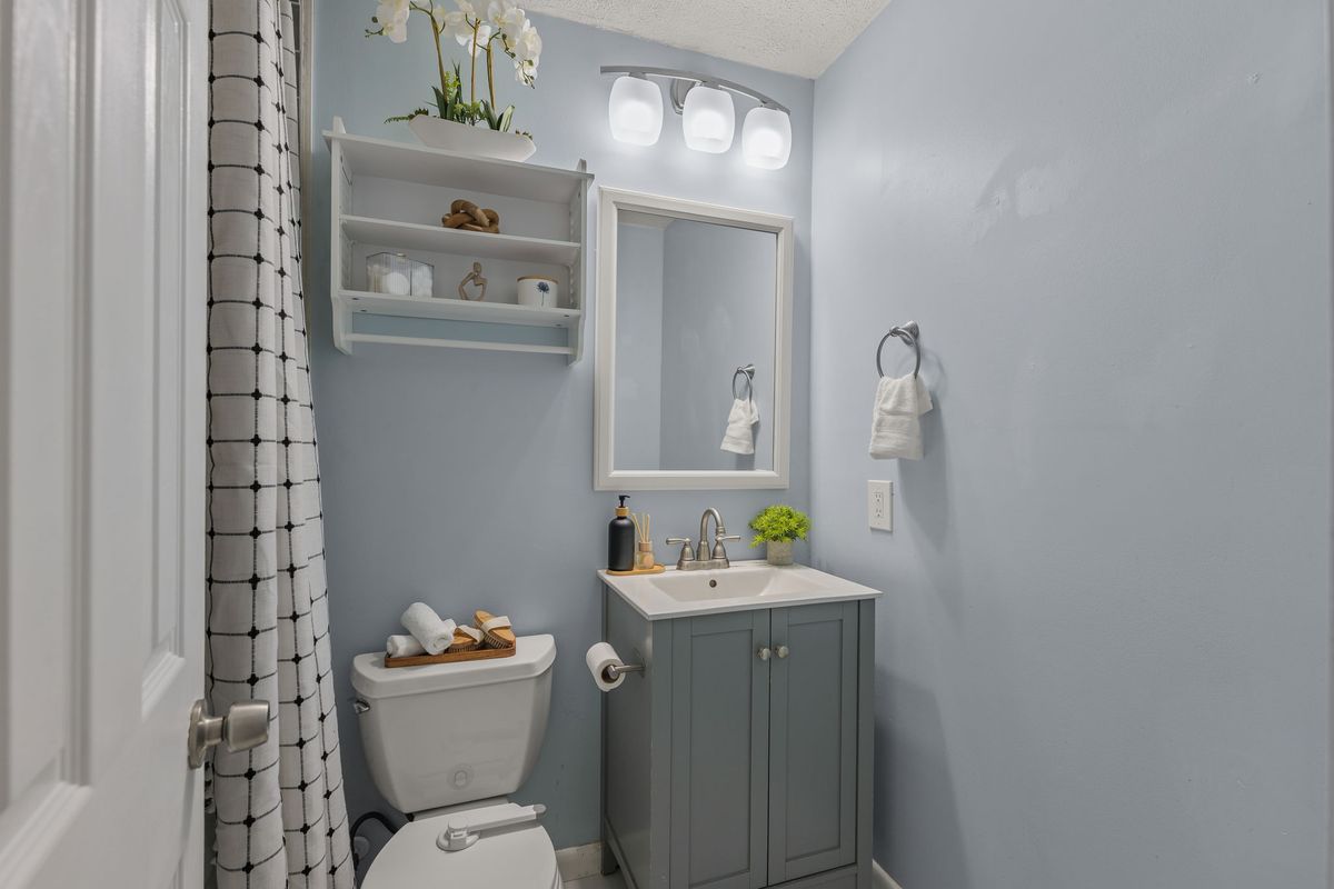 Powder bath with pale blue walls, a gray vanity, a framed mirror and open shelves with white orchids