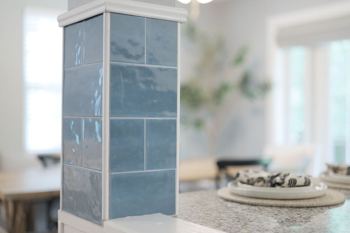 Close-up of a column clad in glossy blue tile beside a granite counter set with plates