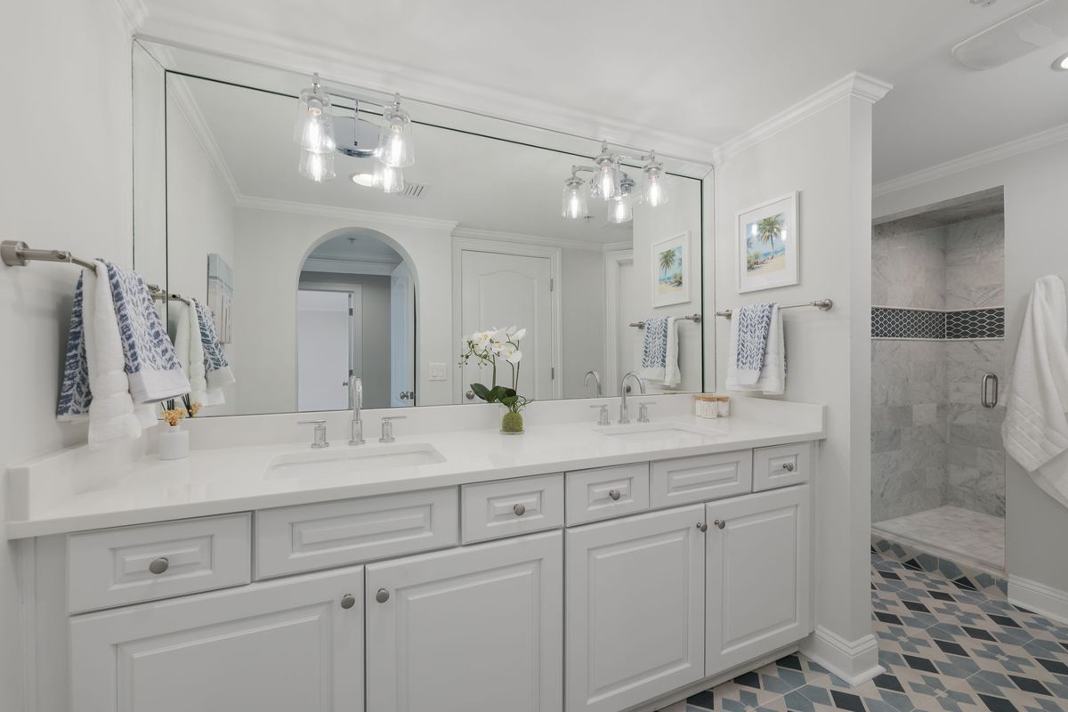 Bathroom with a white double vanity, a wide mirror and a blue and white patterned tile floor