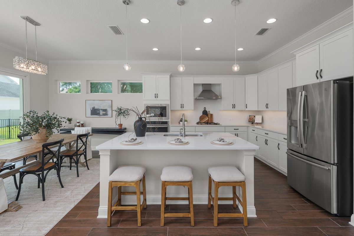 White kitchen with a large island, three wood counter stools and pendant lights, open to a dining area