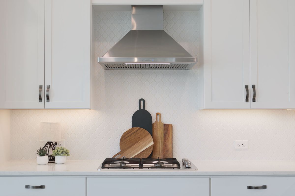 Styled kitchen counter with wooden cutting boards and small plants beneath a stainless range hood